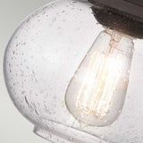 A detailed view of an Edison-style LED filament bulb shining warmly within a clear glass fixture, adorned with a textured water droplet design. The bulb's warm glow accentuates the intricate glass surface, enhancing the classic allure of the Trilogy 1 Light Wall Light in Old Bronze.