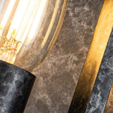 Close-up of the Vanguard 2 Light Wall Light - Old Black, featuring a glowing bulb with a visible filament. The industrial-inspired design is finished in Old Black and stands out against a textured gray surface, highlighting the warm light it emits.