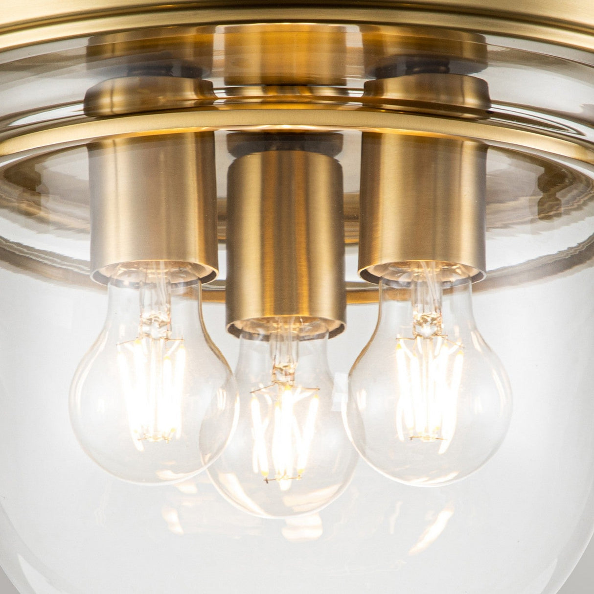 The Whistling 3 Light Flush in brushed brass features two vintage-style LED bulbs within a glass semi-flush ceiling light fixture. Its design incorporates clear glass and brass fittings that highlight the exposed filaments, offering an elegant and modern look ideal for bathroom lighting.