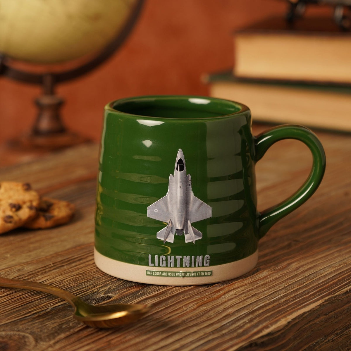 Green ribbed stoneware mug with beige base, printed with a grey F-35B Lightning jet and "LIGHTNING" text, shown beside books, cookies, and a spoon.