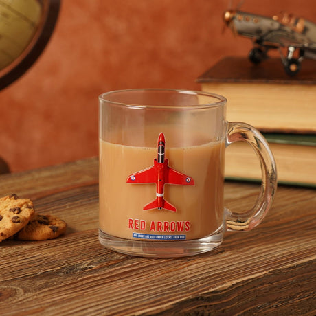 Clear glass mug, 10oz, with a red jet aircraft print and "RED ARROWS" text, filled with tea and set on a wooden surface beside books and cookies.