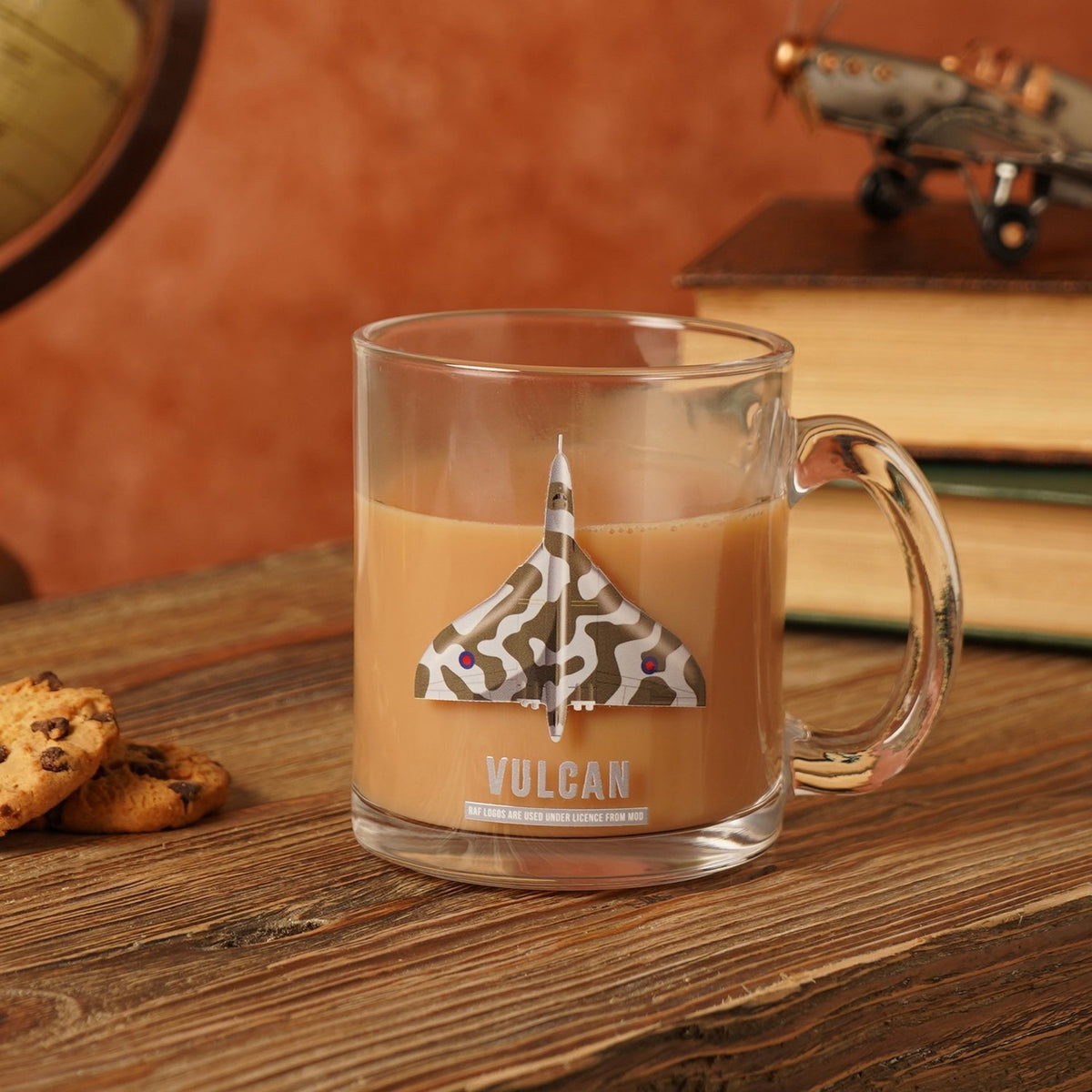 Clear glass Vulcan mug, 10oz, with a camouflage delta-wing aircraft print and "VULCAN" text, shown filled with tea on a wooden surface beside cookies.