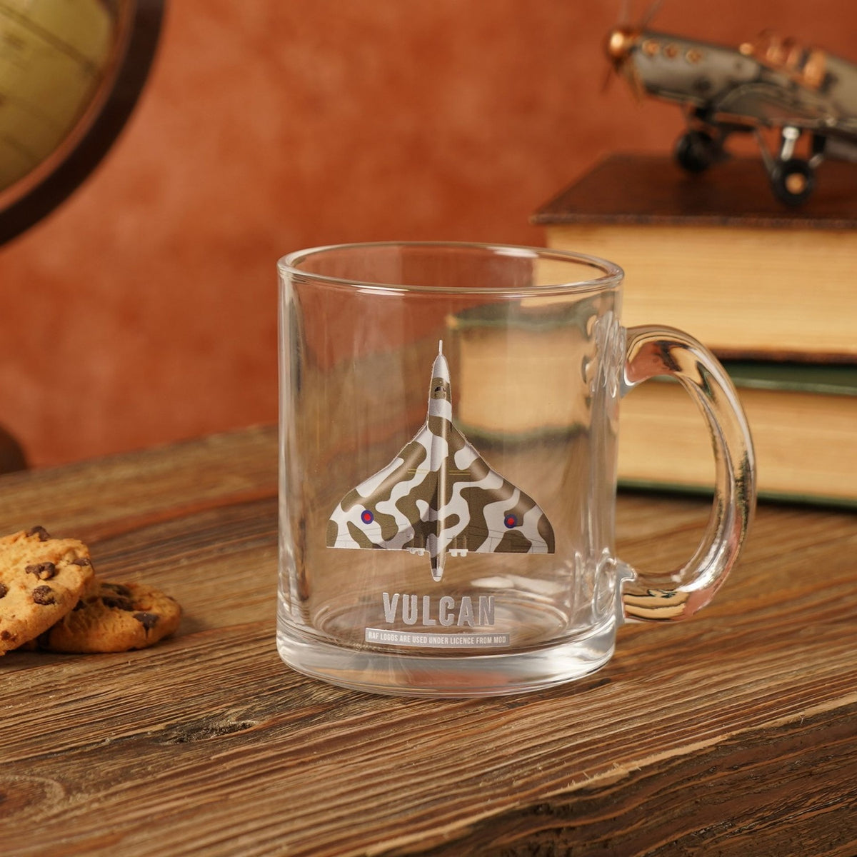 Clear glass mug, 10oz, printed with a camouflage Vulcan delta wing aircraft and "VULCAN" text, shown on a wooden table with books and a model plane.