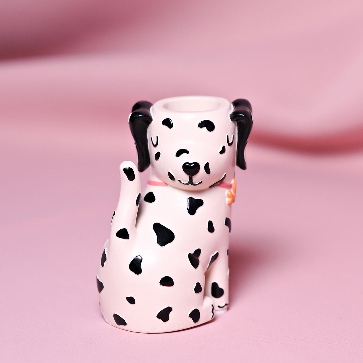 Resin matchstick holder shaped as a seated spotted dog with black ears, closed eyes, and a pink collar, matchstick opening atop its head, on a pink backdrop.