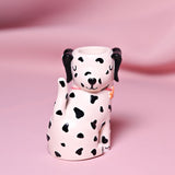 Resin matchstick holder shaped as a seated spotted dog with black ears, closed eyes, and a pink collar, matchstick opening atop its head, on a pink backdrop.