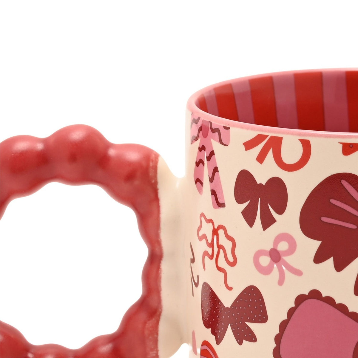 Close-up of a porcelain mug with a chunky red bobble-shaped handle, cream body patterned with pink and burgundy bows, and red-and-pink striped interior, shown on a white background.