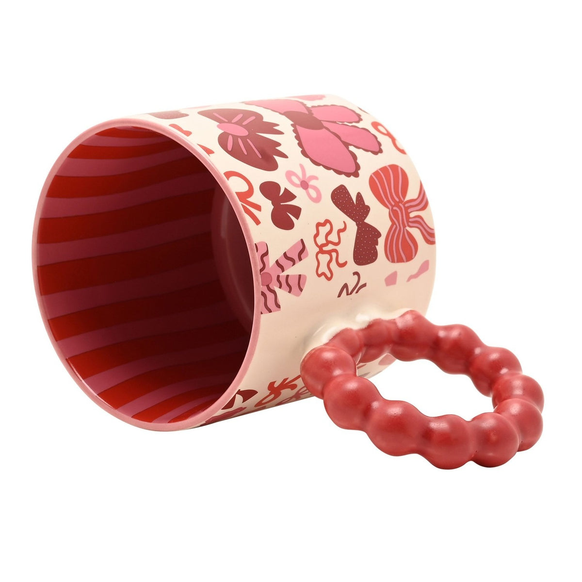 Porcelain mug lying on its side showing a red striped interior and a chunky bobble-style red ring handle, with a cream exterior patterned in pink and burgundy bows, on a plain white background.