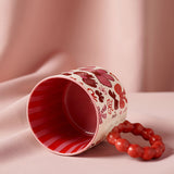 Porcelain mug with bows pattern in red and pink on a cream body, red striped interior, and a chunky bobble-ring red handle, shown tipped on its side against a pink fabric backdrop.