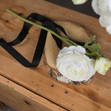 Hill Interiors White Ranunculus Spray with layered bloom and bud on a birch wood slice with black ribbon, styled on a rustic pine surface.