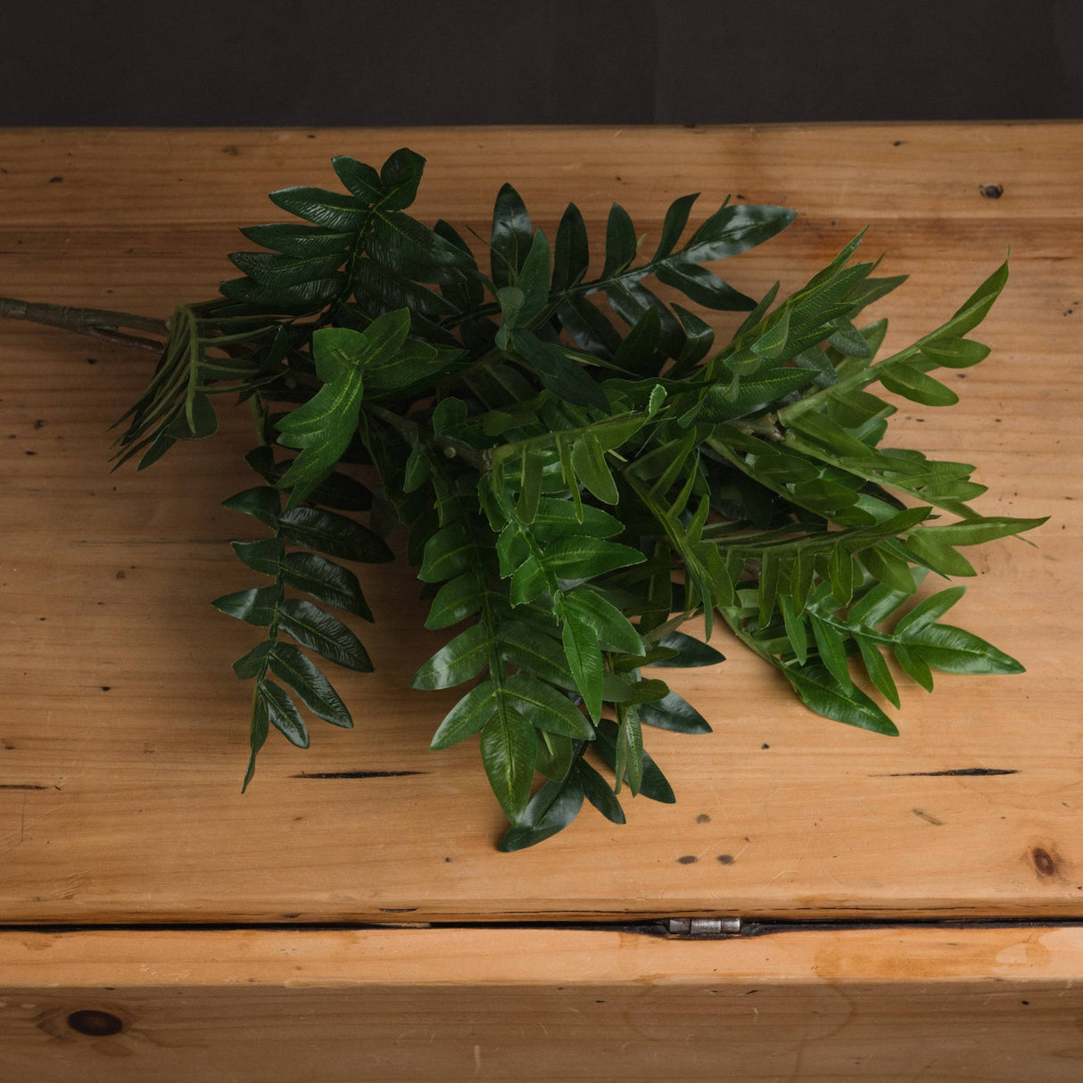 Hill Interiors Pistach Bunch faux foliage stem with clusters of rounded green pistachio-style leaves, displayed on a light wooden surface.