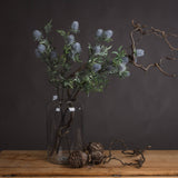 Hill Interiors Eryngium Thistle faux stems with grey cone heads and green bracts in a glass jar with twisted branches and pine cones.
