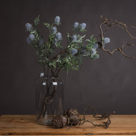 Hill Interiors Eryngium Thistle faux stems with grey cone heads and green bracts in a glass jar with twisted branches and pine cones.