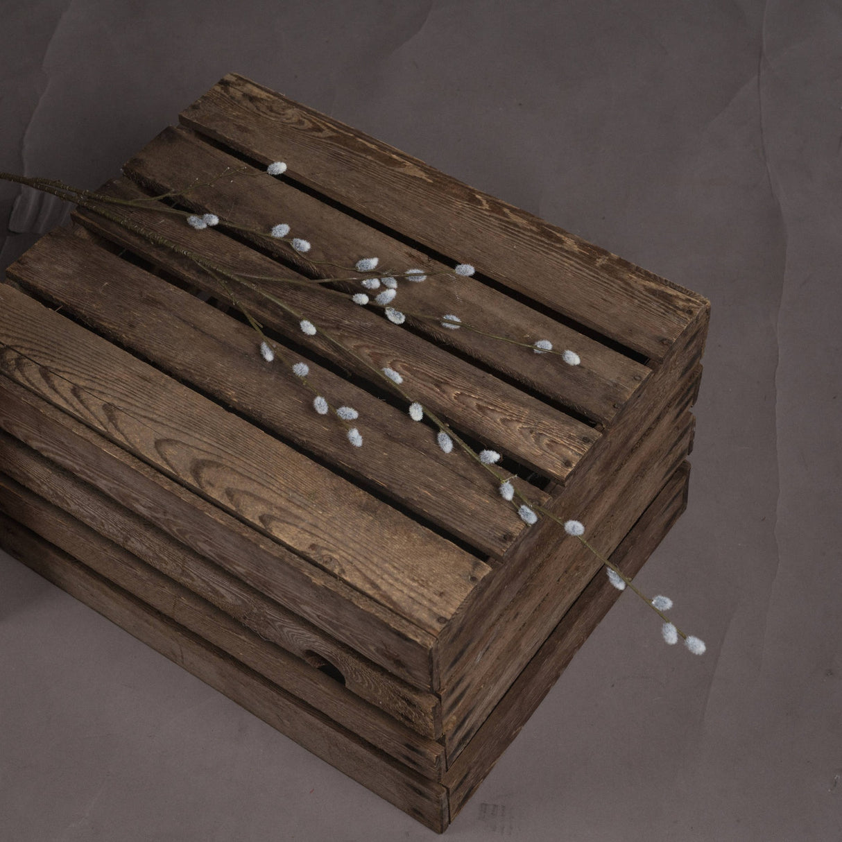 Hill Interiors Pussy Willow Branch, a faux foliage stem with downy white buds, laid across a rustic slatted wooden crate on a grey backdrop.