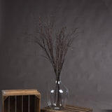 Hill Interiors Branch Spray faux foliage in tall brown twisted twigs arranged in a clear glass vase atop a wooden crate against a grey backdrop.
