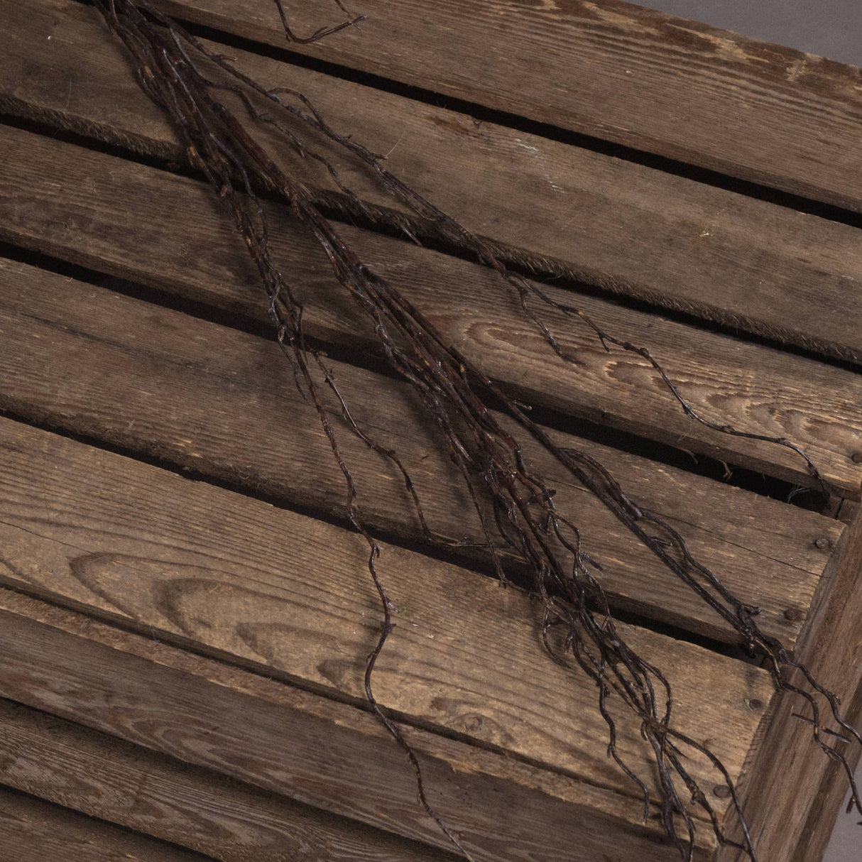 Hill Interiors Branch Spray faux foliage stem with slender brown twigs resting across weathered wooden slats.