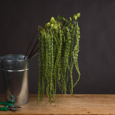 Hill Interiors Green Amaranthus faux stem with cascading beaded plumes displayed in a galvanised metal bucket on a wooden surface against a dark background.