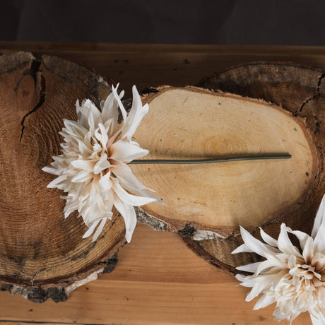 Hill Interiors Café Au Lait faux dahlia stem with a ruffled cream and soft peach bloom, resting on rustic log slices.
