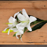 Hill Interiors White Lily faux flower stem with open white blooms, buds, and green veined leaves, displayed on a light wooden surface.