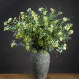 Hill Interiors Sweet Pea Trail faux stems with ruffled green blooms and trailing foliage arranged in a weathered grey stone vase against a dark background.