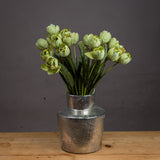 Hill Interiors Green Tulip faux stems arranged in a hammered silver metal vase on a wooden surface against a dark grey background.