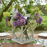 Lush floral arrangement with purple hydrangeas, white lilies, green blooms and Hill Interiors cream gardenia stems in a white lantern vase on an outdoor table.