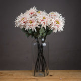 Hill Interiors Lush Pink Dahlia faux stems arranged in a tall clear glass vase on a wooden surface against a dark grey background.