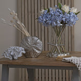 Hill Interiors light blue large headed agapanthus arranged with white proteas in a glass vase with starfish base, styled beside coral and a silver vase on wood.