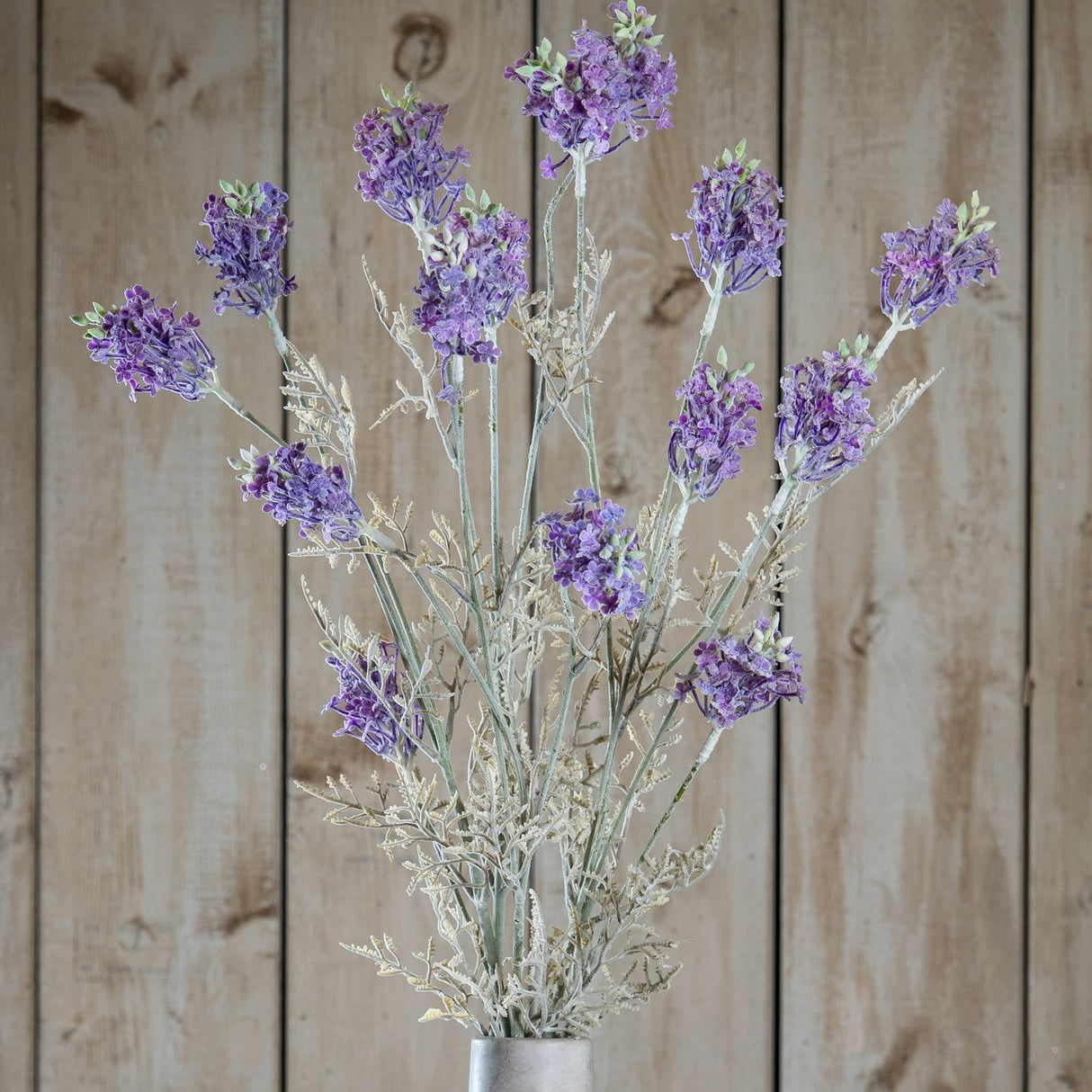 Hill Interiors Purple Meadow Flower stems with clustered ruffled purple blooms and pale green foliage, displayed against a light wooden plank background.