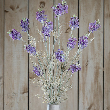 Hill Interiors Purple Meadow Flower stems with clustered ruffled purple blooms and pale green foliage, displayed against a light wooden plank background.