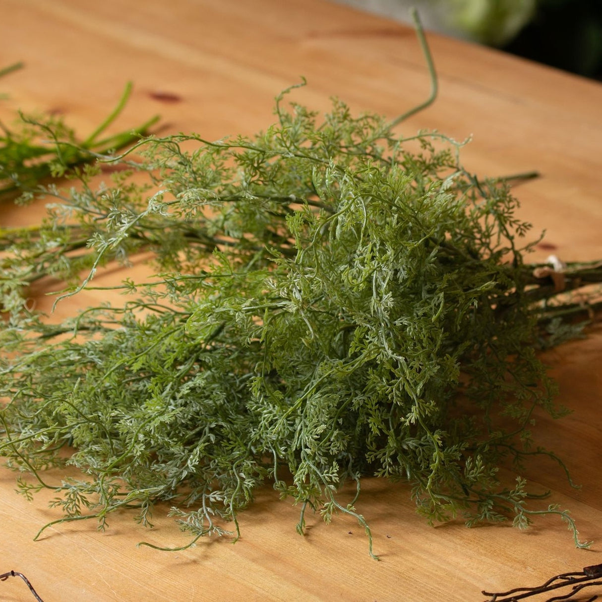 Hill Interiors Asparagus Fern Bunch with fine green feathery fronds and bendable plastic stems, laid on a wooden surface.