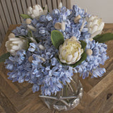 Hill Interiors dried white bunny tail stems styled with blue hyacinths and white protea in a starfish glass vase on a wooden table.