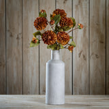 Hill Interiors Deep Mustard Dahlia Stem arranged with layered rust blooms and green leaves in a tall matte grey bottle vase against wood panelling.