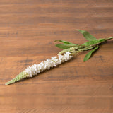 Hill Interiors White Veronica Stem laid diagonally on a wooden surface, showing the tapering spire of small white blooms and slim green leaves.