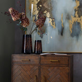 Hill Interiors Burgundy Rosehip Stem with red berries and hydrangea blooms in a dark tortoiseshell vase on a wooden sideboard beside abstract gold artwork.