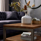 Hill Interiors Bouquet of Dried Tall Thistle in a white ceramic vase on a rustic wood coffee table, styled beside a grey tufted velvet sofa.
