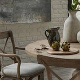 Hill Interiors Real Touch Artificial Artichokes styled on a wooden board atop a round dining table with a ceramic jug and stone vase.