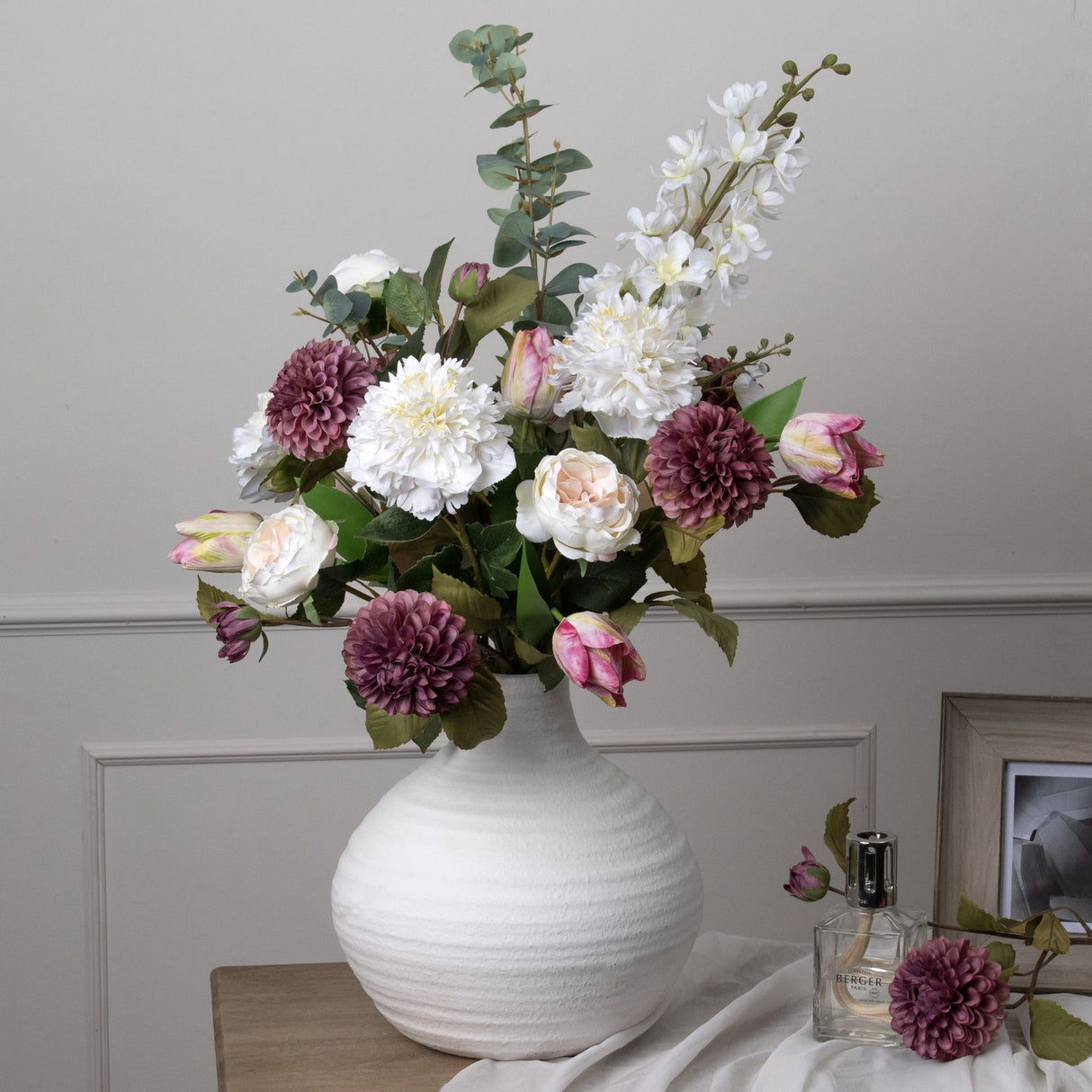 Hill Interiors Tall White Delphinium Stem arranged with white peonies, mauve dahlias, pink tulips and eucalyptus in a textured white ceramic vase.