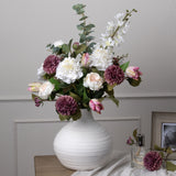 Hill Interiors Tall White Delphinium Stem arranged with white peonies, mauve dahlias, pink tulips and eucalyptus in a textured white ceramic vase.