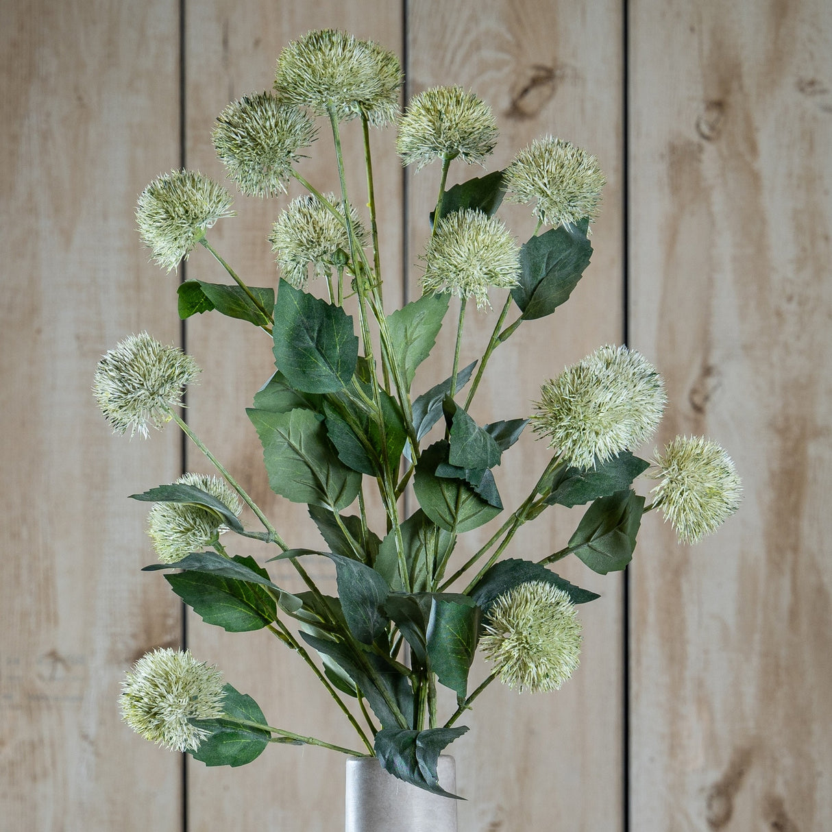 Hill Interiors Thistle Globe Stem faux plant with spiky green globe heads and leafy stems arranged in a vase against a wooden plank background.