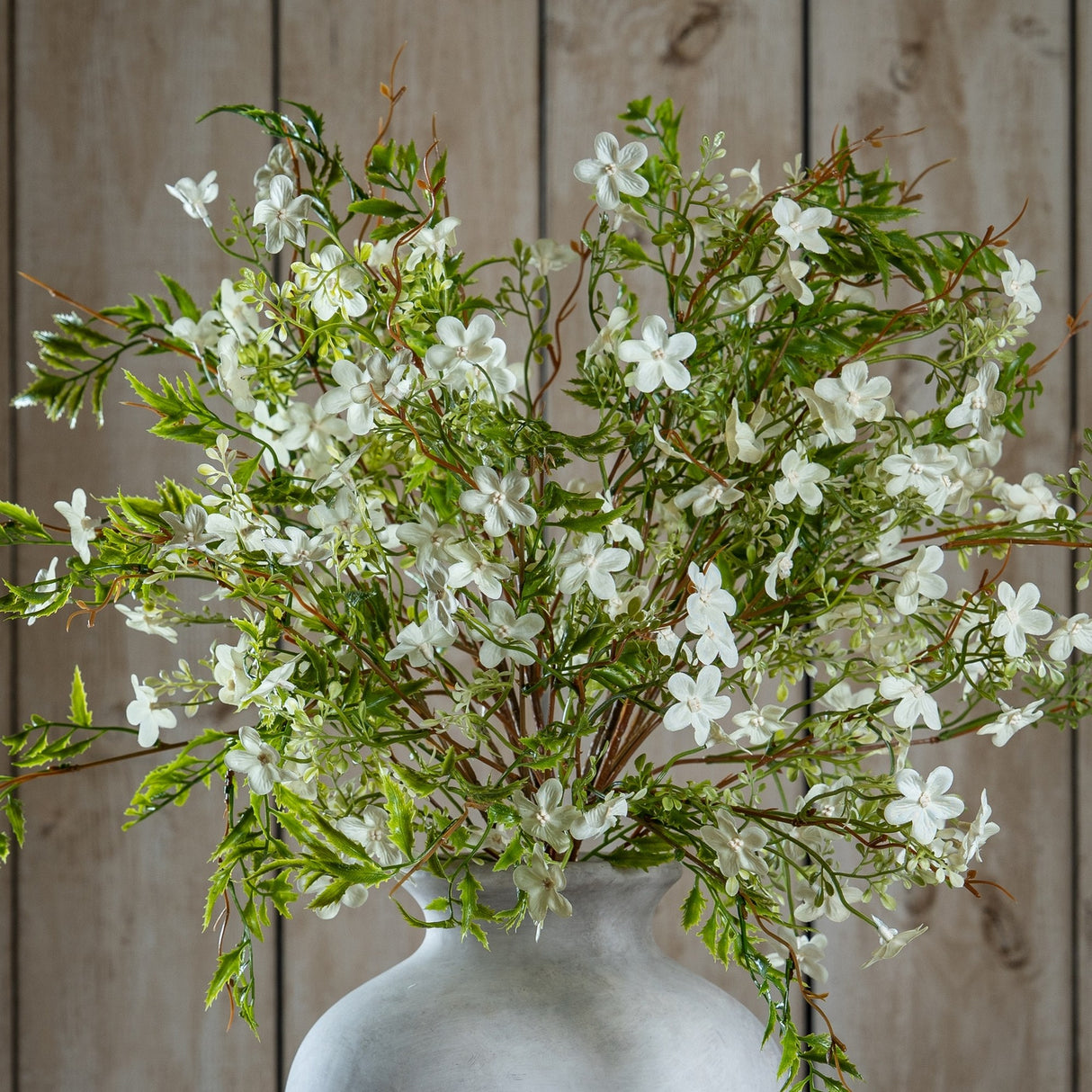 Hill Interiors Italian White Bellflower faux stems with clusters of small white blooms and green foliage, arranged in a stone vase against wood panelling.