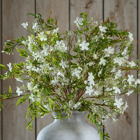 Hill Interiors Italian White Bellflower faux stems with clusters of small white blooms and green foliage, arranged in a stone vase against wood panelling.
