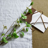 Tall Mock Orange Spray by Hill Interiors laid on white linen beside an open leather-bound journal and pencil, showing white blossoms and green leaves.