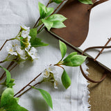 Hill Interiors Tall Mock Orange Spray with white blossoms and green leaves laid beside a brown leather-bound journal on linen fabric.
