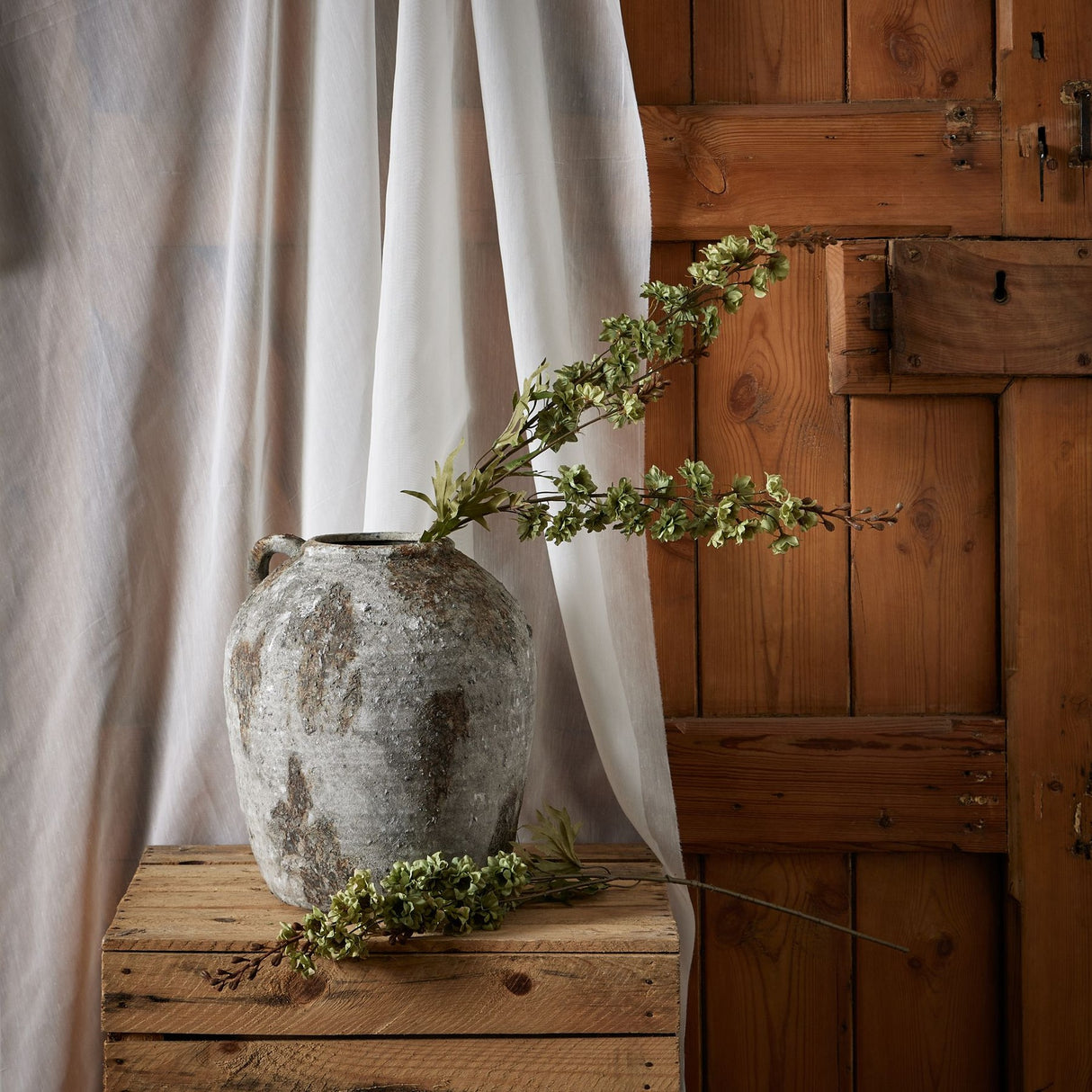Hill Interiors Tall Green Hops Stem displayed in a weathered stone jug on a rustic wooden crate, with a second stem resting alongside against linen drapery.