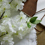 Hill Interiors Large White Full Cherry Blossom Stem with clustered white blooms and green leaves, styled beside a brown leather journal on linen.