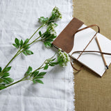 Hill Interiors Faux White Cow Parsley Ammi stems with delicate white florets and green foliage, laid on white linen beside a leather-bound journal and pencil.