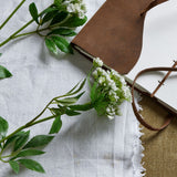 Faux white cow parsley ammi stem by Hill Interiors with lace-cap florets and green foliage, styled beside a brown leather journal on white linen.