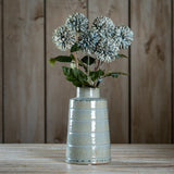 Hill Interiors White Chrysanthemum faux stems arranged in a glossy pale ceramic ribbed vase on a wooden surface against a plank wall.