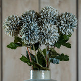 Hill Interiors Pale Green Blue Short Chrysanthemum faux stems with layered petals and green leaves, arranged in a speckled ceramic vase against pale wood.