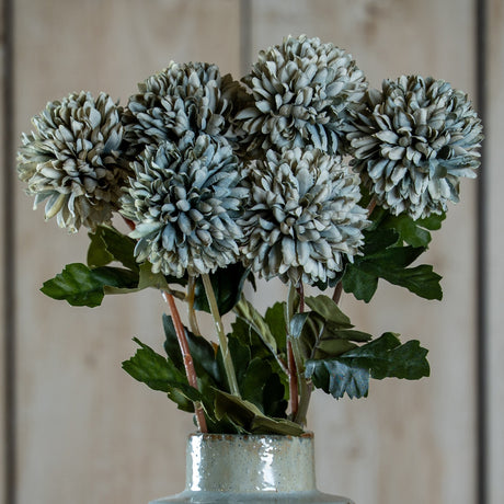 Hill Interiors Pale Green Blue Short Chrysanthemum faux stems with layered petals and green leaves, arranged in a speckled ceramic vase against pale wood.